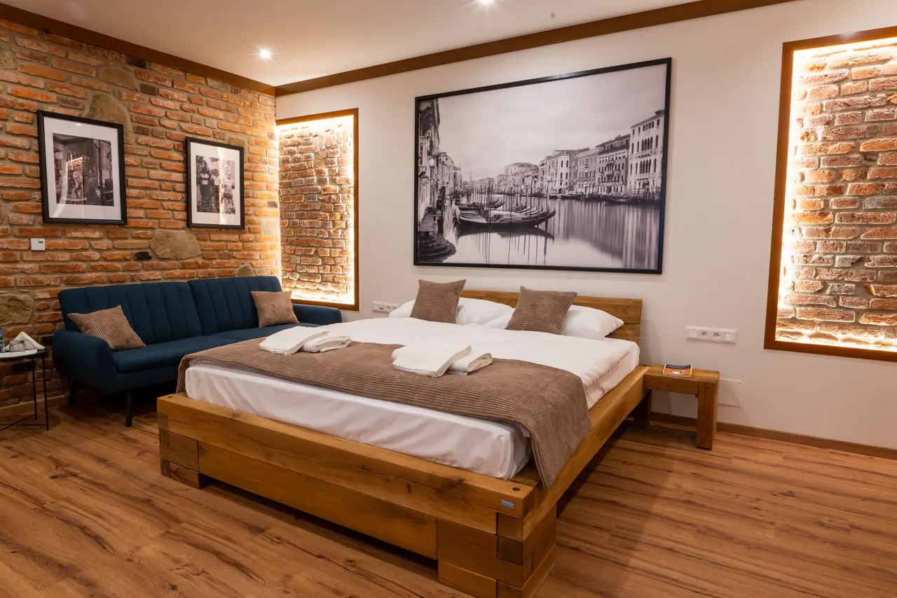Pokój Superior King w Penzión Kolkáreň, Stará Ľubovňa — niebieska sofa, drewniane łóżko i podświetlane ceglane wnęki